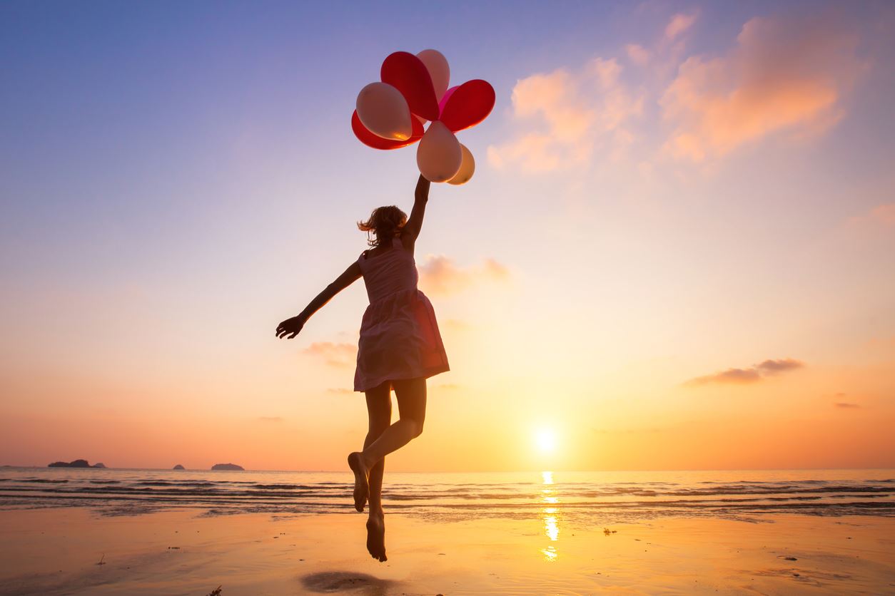 ragazza in riva al mare con palloncini in mano al tramonto